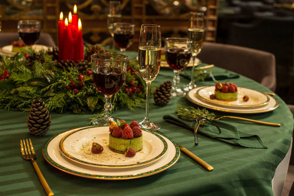 Новогодняя композиция на столе, свечи, пирожные на тарелках, бокалы с напитками, столовые приборы