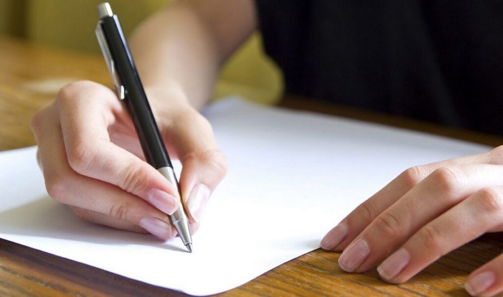 Ручка в руке и лист бумаги на столе