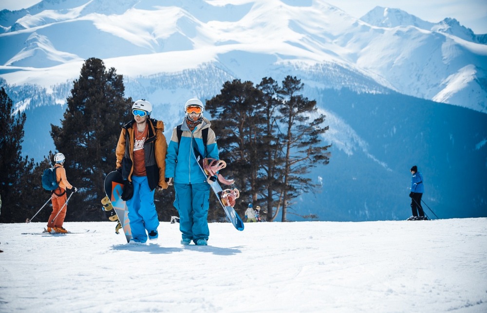 Люди в горнолыжных костюмах со сноубордами, горы, деревья, снег