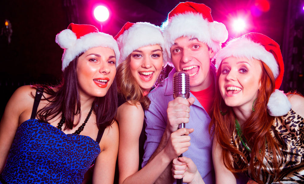 Молодой человек и девушки в новогодних колпаках, микрофон в руках