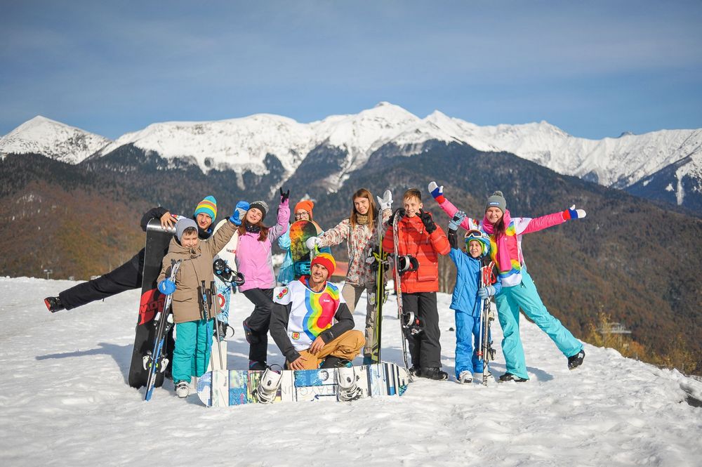 Взрослые и дети в горнолыжных костюмах со сноубордами на снегу на фоне горы