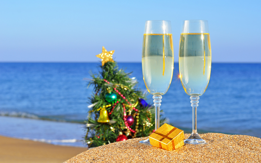 Бокалы с шампанским на пляже, наряженная елка возле моря