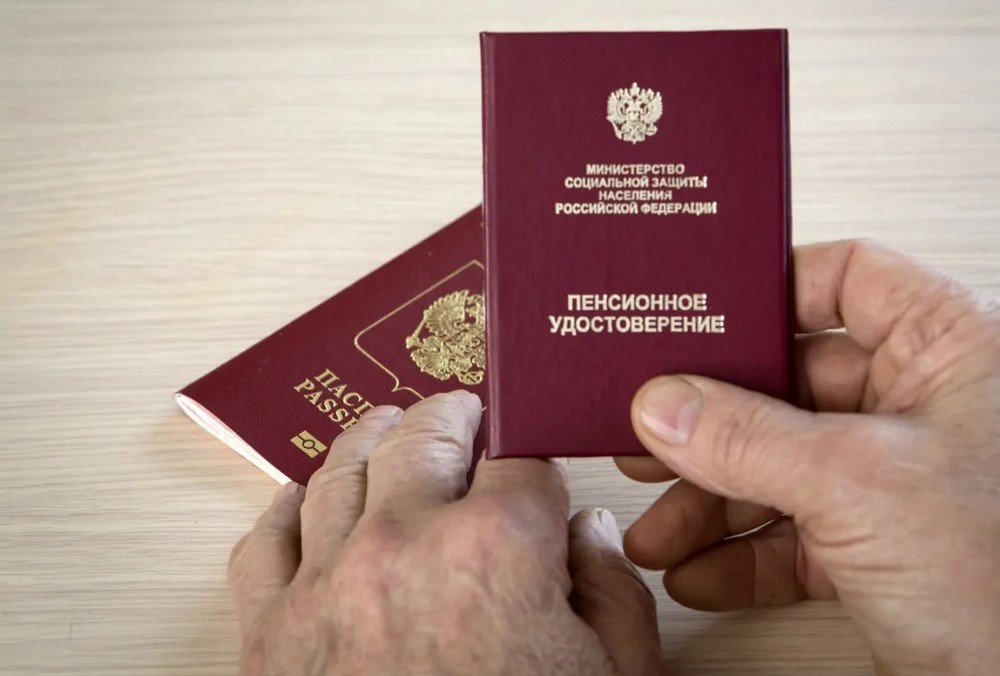 Пенсионное удостоверение в руке и паспорт на столе